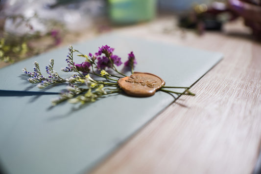 green envalope with a golden wax seal infused with dried green and purple flowers